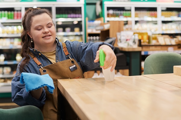 Portrait à la taille d'une jeune femme handicapée souriante travaillant dans un supermarché et désinfectant des tables dans un café.