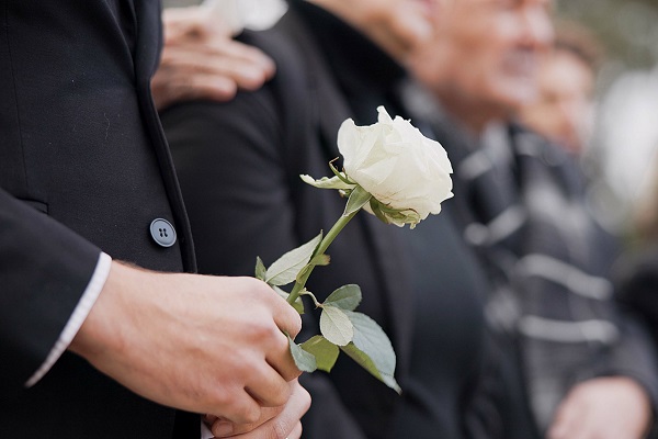 Les mains, une rose et une personne lors d'un enterrement dans un cimetière en deuil lors d'un service commémoratif. Mort, fleur et un adulte en costume dans un cimetière dans une foule pour un enterrement en plein air gros plan.