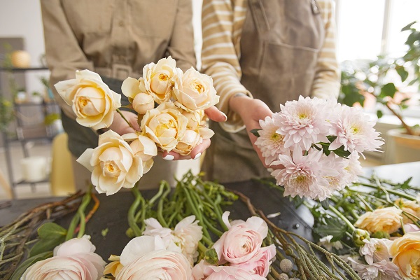 Vue en plongée de belles fleurs sur une table dans un magasin de fleurs avec deux fleuristes méconnaissables arrangeant des bouquets