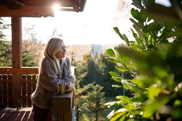 Une femme est debout sur son balcon avec une tasse de café dans la main et regarde le paysage