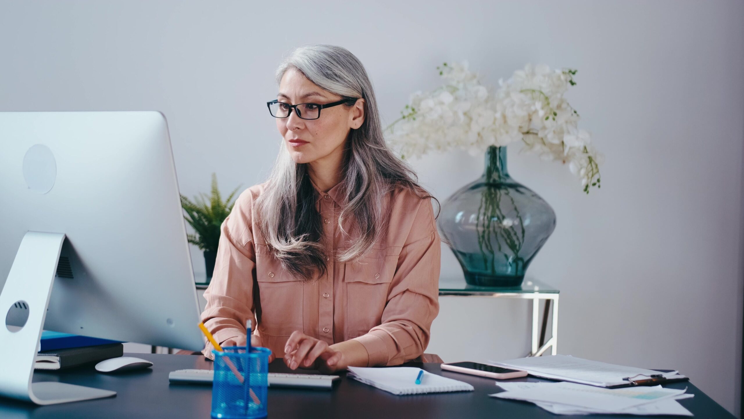 femme sénior qui travaille a son bureau et prend des notes sur son ordinateur