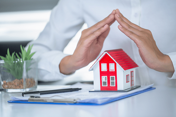 main d'un homme au dessus d'une figurine de maison
