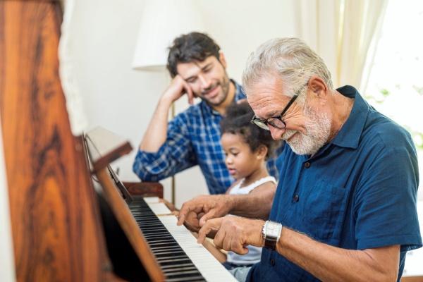 une petite fille joue du piano avec son grand père dans le salon