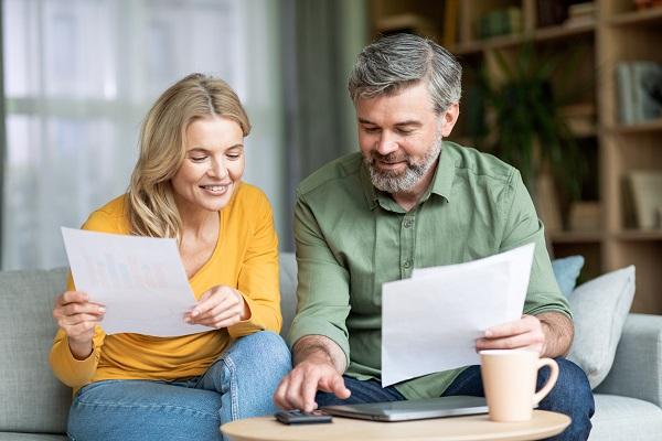 Un couple de quadragénaires calcule et regarde des documents assit dans le canapé