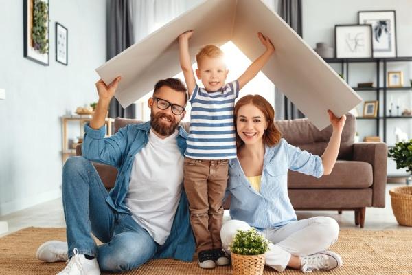 un couple et leur enfant sont assis sur un tapis avec un carton en forme de toit sur leur têtes