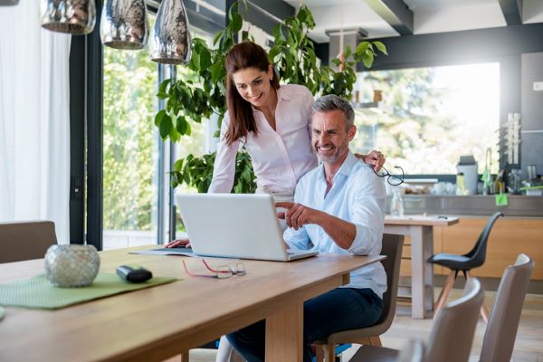 Un couple heureux regarde l’écran d’un ordinateur portable à la table de leur maison